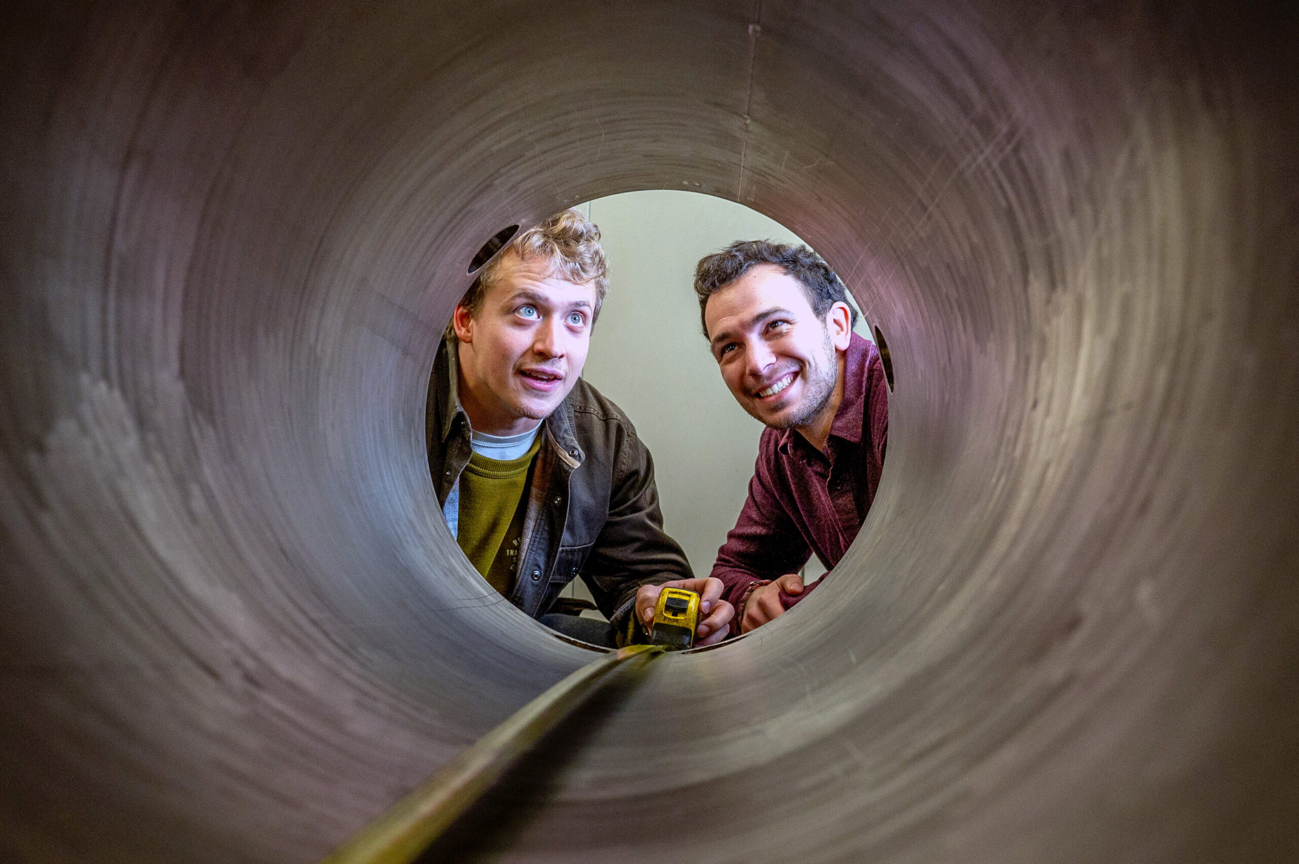 Researchers looking through a large pipe with measuring tape down the length of pipe.