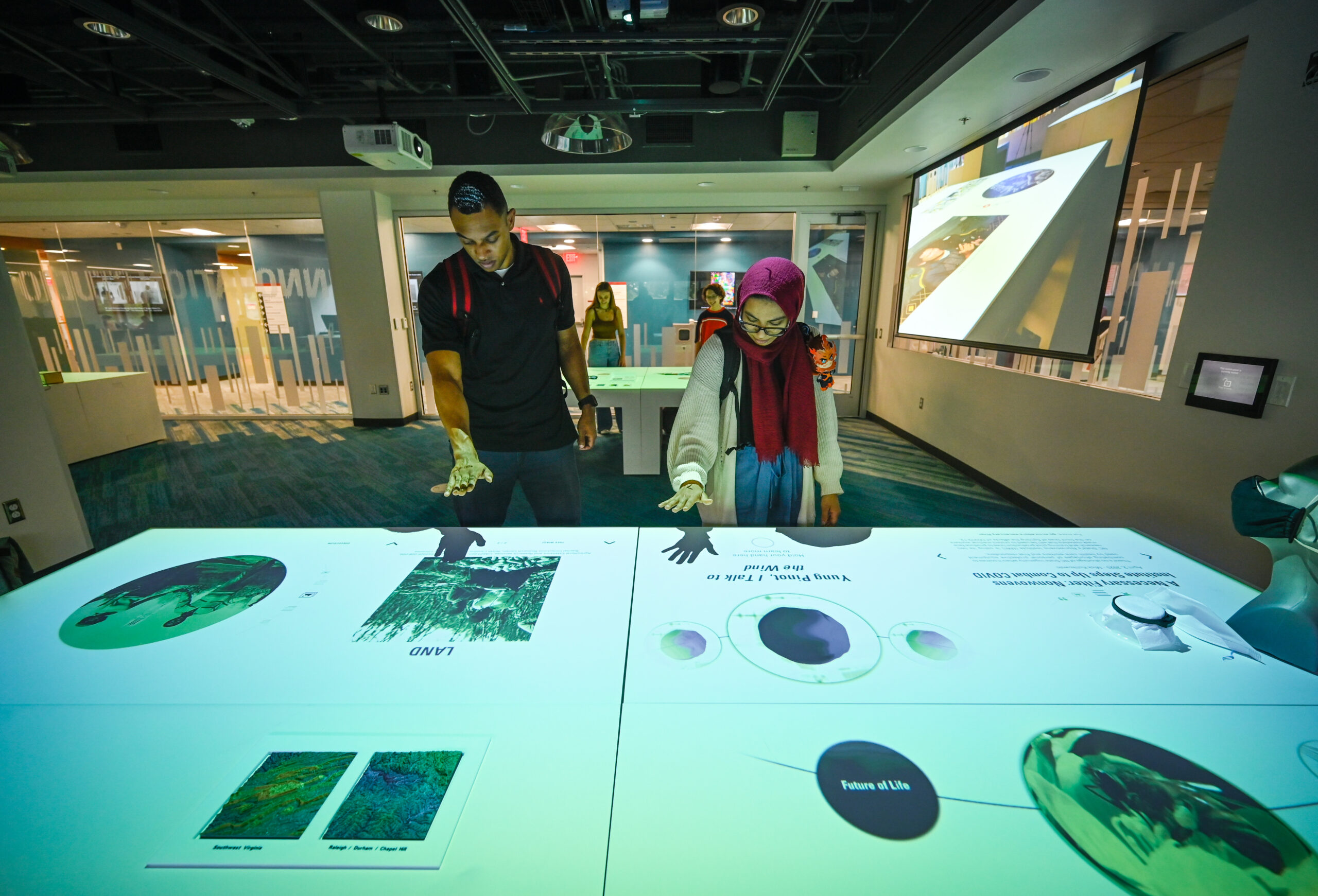Students interacting with the tables in the innovation studio where images are projects onto tables and sensors detect visitors' hand movements to move and engage with the displayed images.